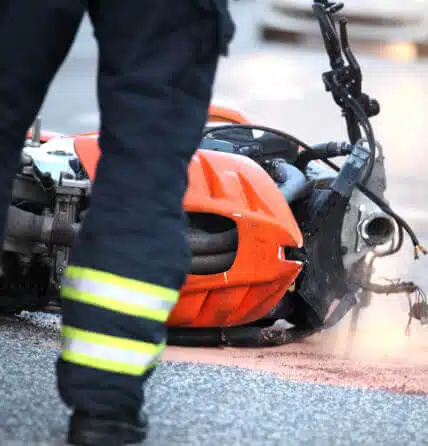 Close up image of a motorcycle on it's side in the road after what appears to be an accident as you see legs of firefighters
