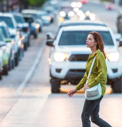 A woman crossing the street with a lot of cars behind her.