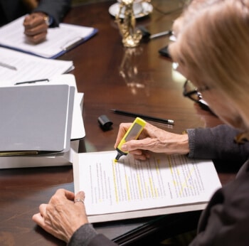 A woman sitting at a desk highlighting some paperwork