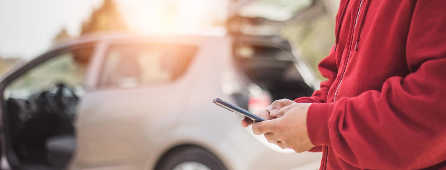 A close up of a mans hand with a cell phone in front of a car